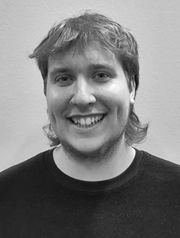 Porträtfoto von Linus Hencke mit mittellangen Haaren und einem breiten Lächeln. Er trägt ein dunkles T-Shirt. Das Bild ist in Schwarz-Weiß aufgenommen.