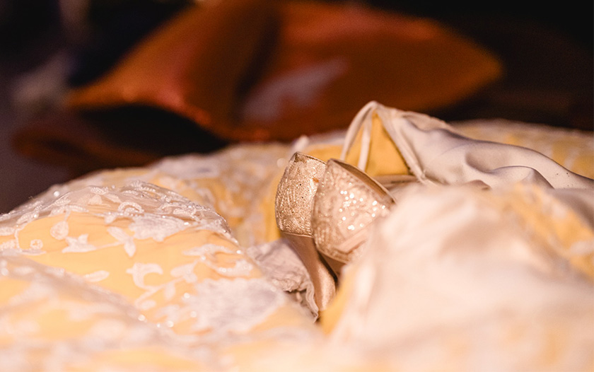 Ein detaillierter Blick auf ein prächtiges Bühnenkostüm von Theater Liberi in sanften Gelb- und Cremetönen mit feinen Spitzenapplikationen. Im Zentrum liegen goldene Glitzerschuhe, eingebettet in die Stofflagen, die auf einen romantischen oder märchenhaften Charakter hindeuten.